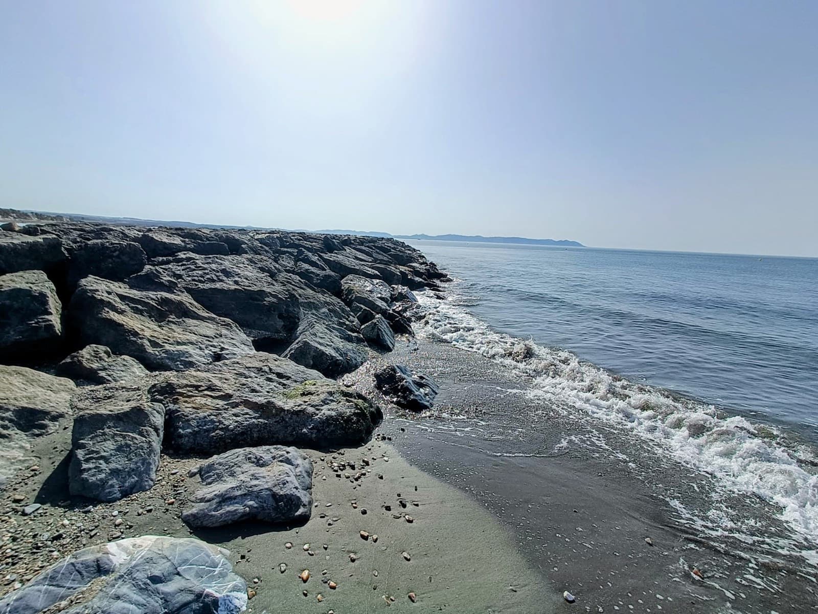 Escollera de rocas junto al mar en un día despejado, con la costa al fondo