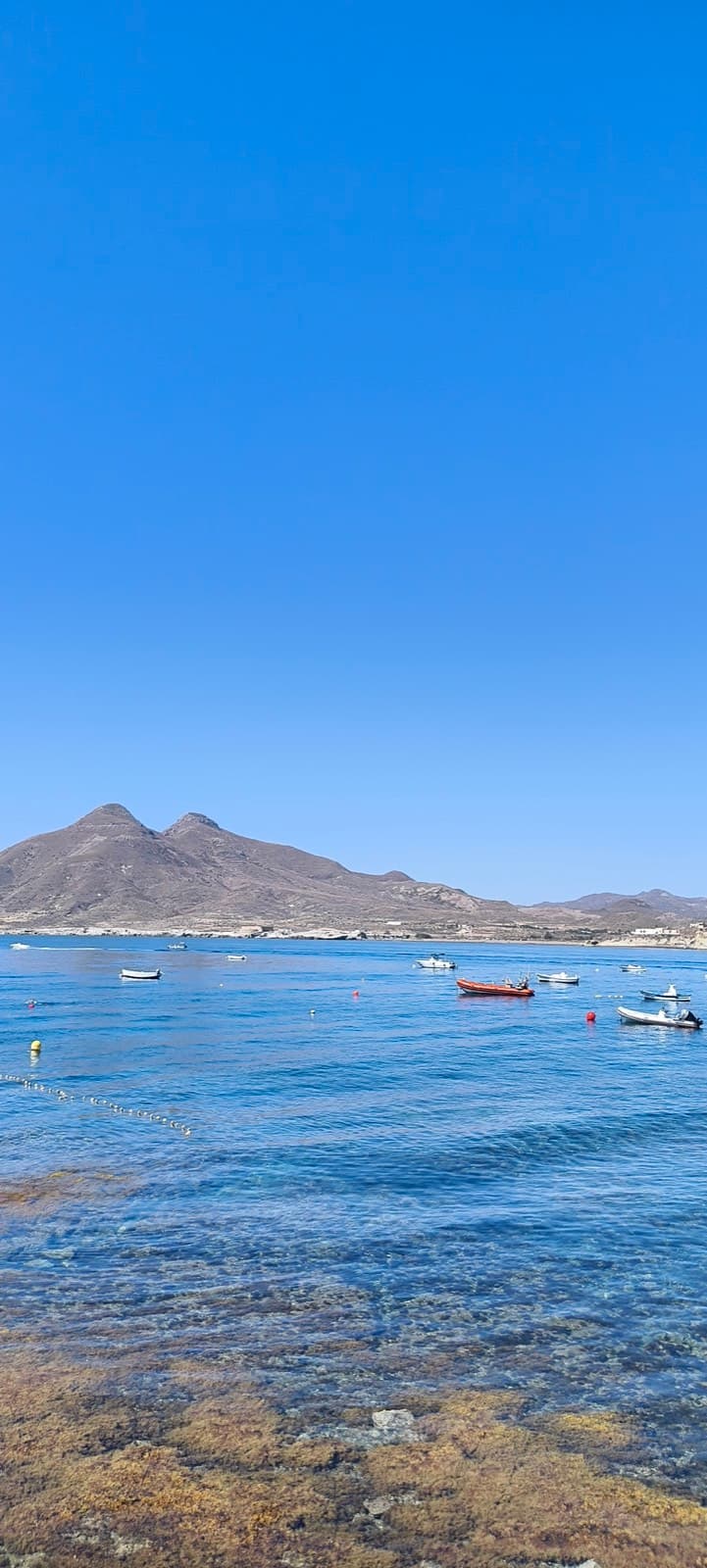 Cala de aguas turquesas con barcas fondeadas y una montaña de doble pico al fondo