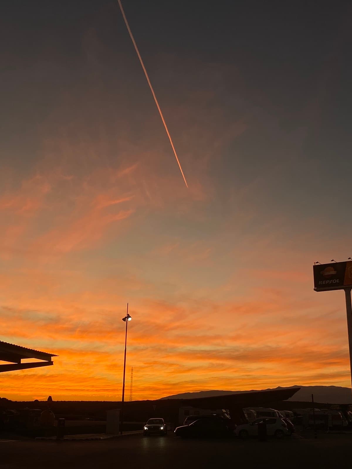 Cielo anaranjado al anochecer surcado por la estela de un avión